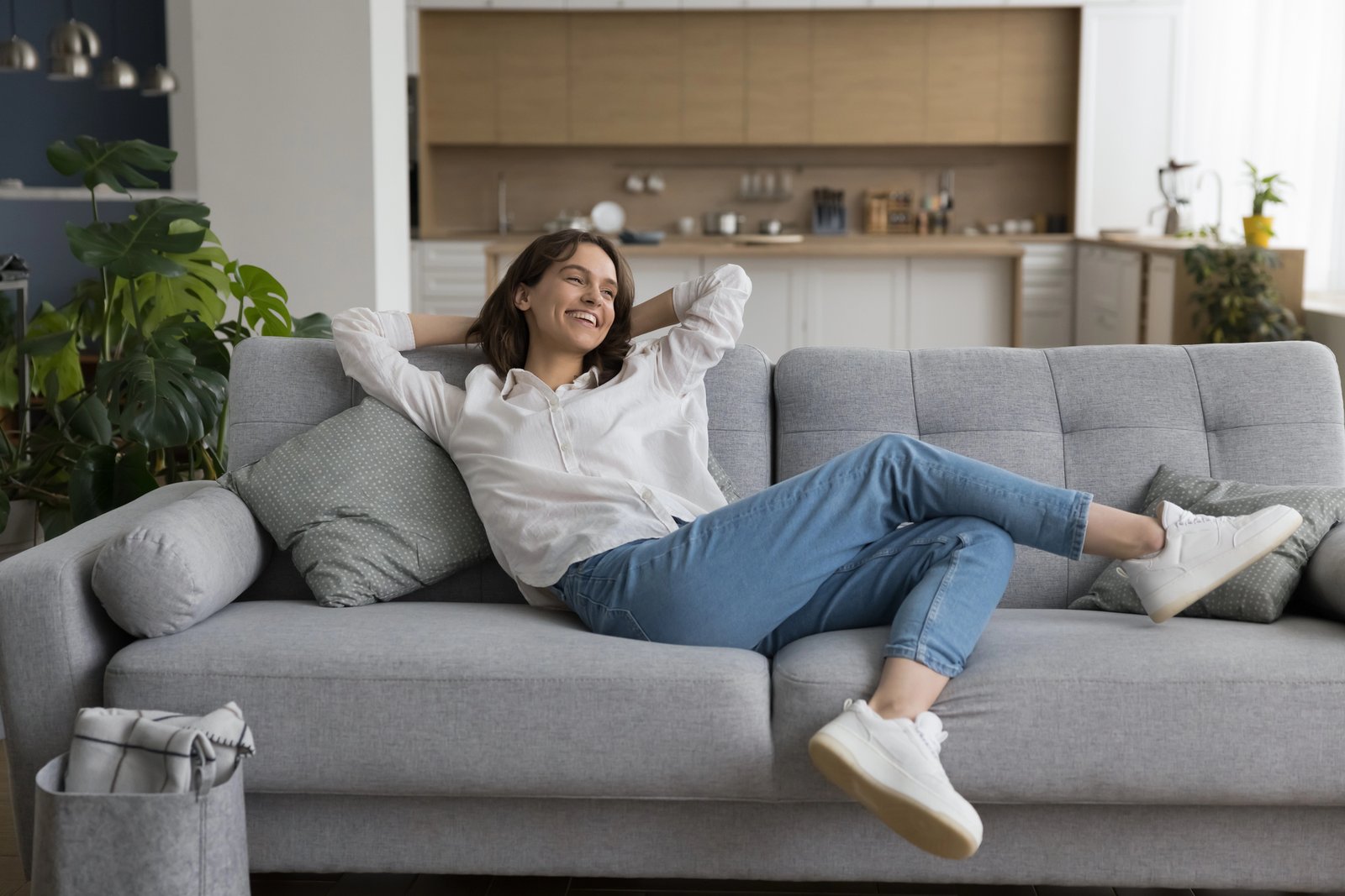 A young woman relaxing happily on a couch in her bright, comfortably furnished home
